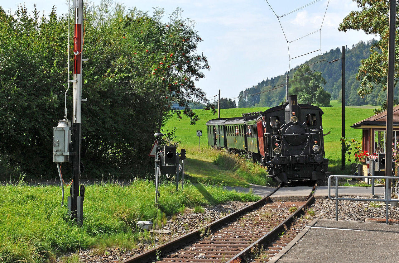 Alte Dampflokomotive fährt an einem Bahnübergang vorbei