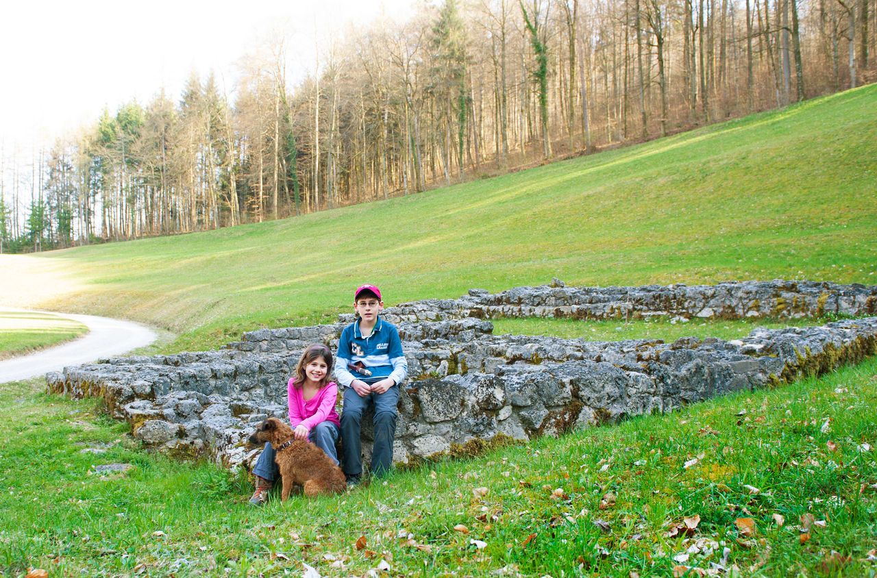 Zwei Kinder und ein Hund sitzend auf einer alten Ruine