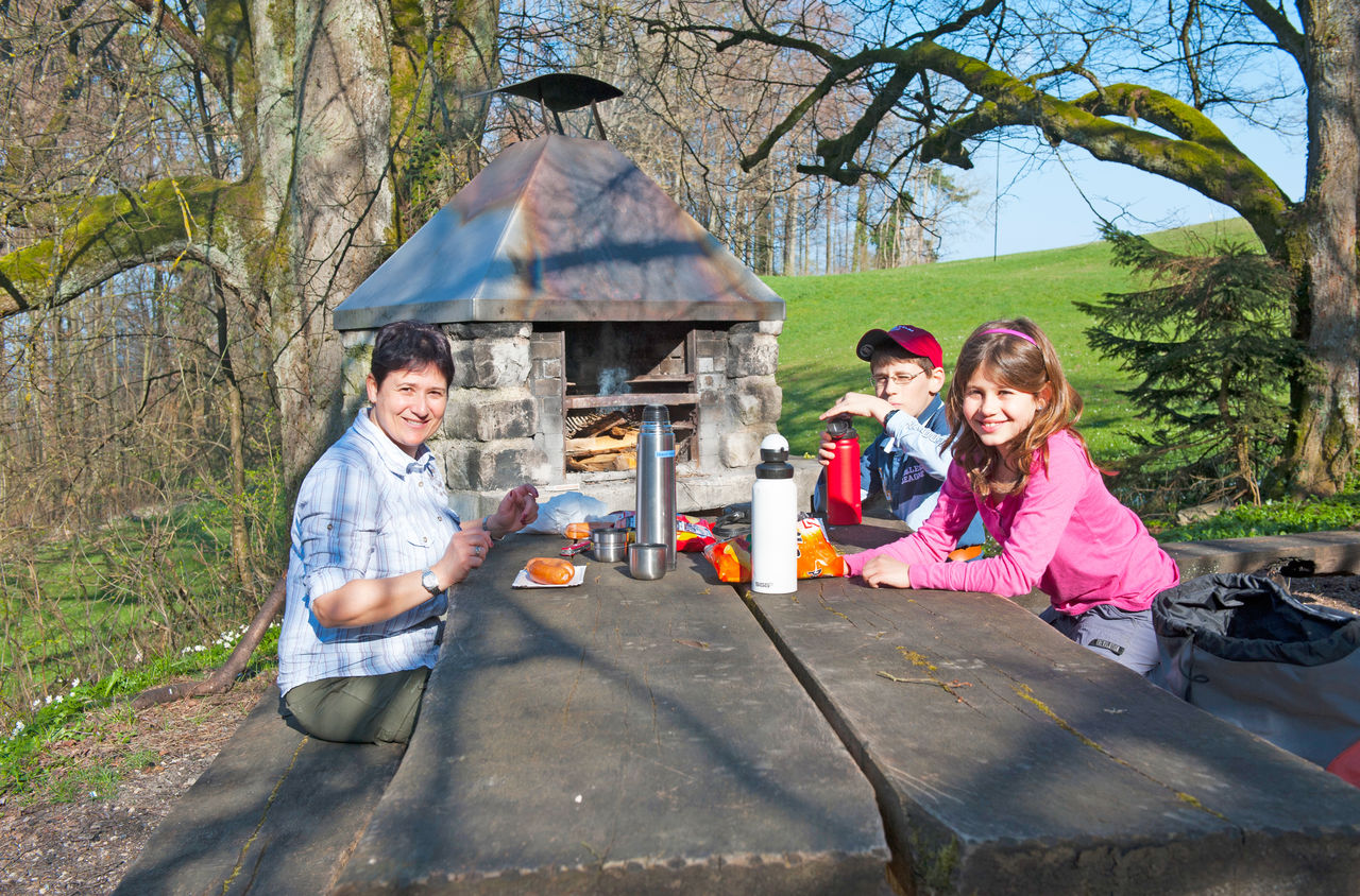 Eine Frau mit zwei Kindern Picknickt an einem massiven Holztisch